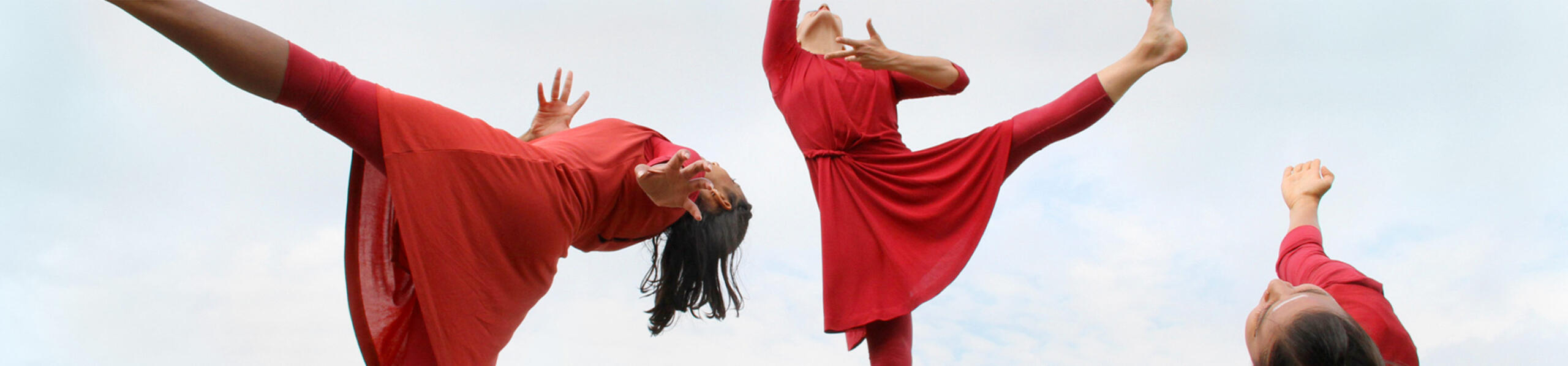 three dancers caught mid-motion in red dance costumes agains the sky