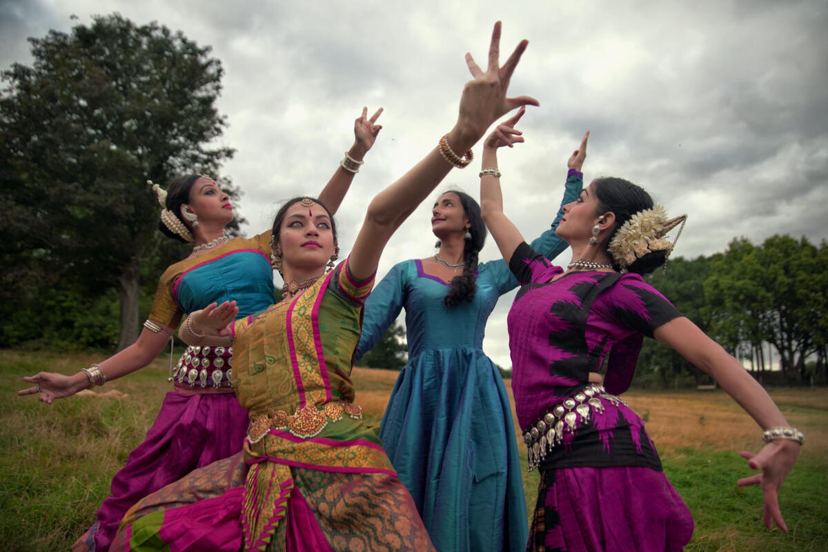 four female Indian Classical dancers dressed in colourful costume and striking a pose in a green area