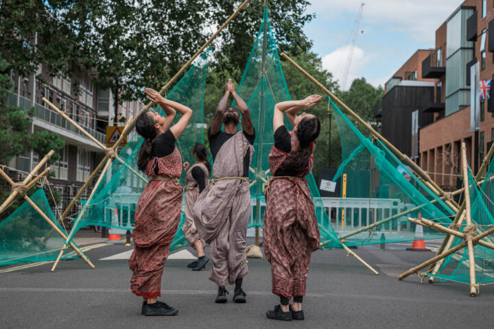 three artists striking a dance pose against bamboo and net structures