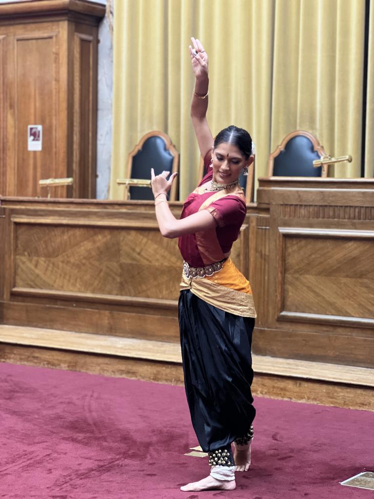 A Bharatanatyam artist dressed in Black silk bottoms and red silk top striking a standing side pose.